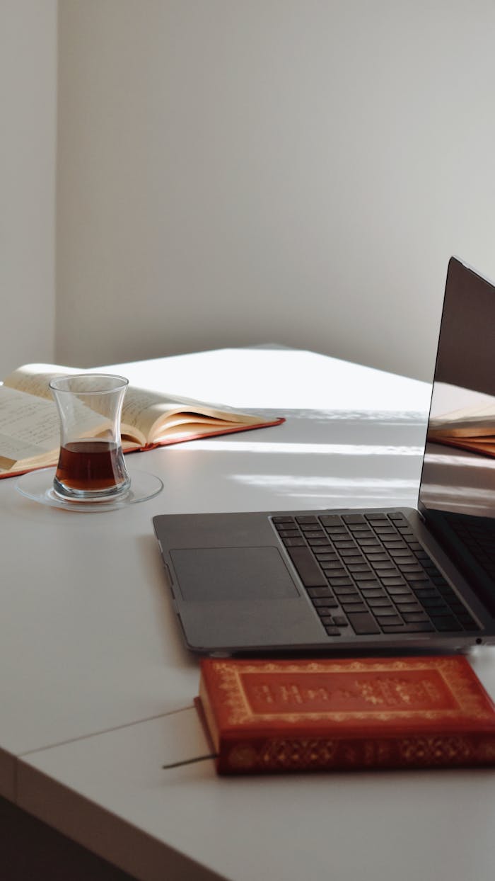 A serene home office setting with a laptop, tea, and books on a white table.