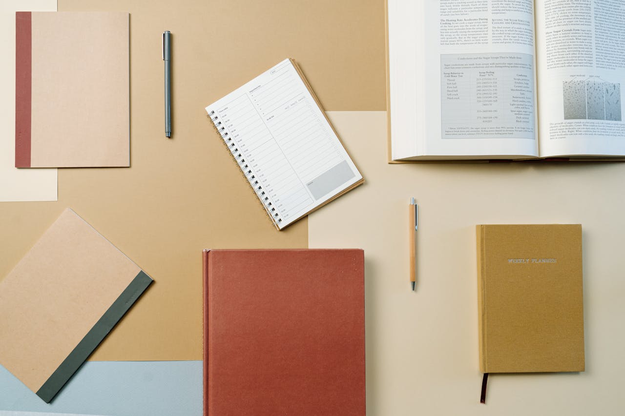 A neatly arranged flat lay of textbooks, notebooks, and stationary items on a brown background.